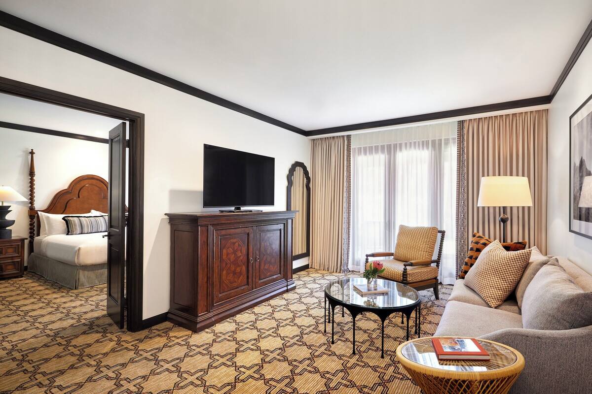 Hotelkamer met een bed, televisie, bank, stoel, salontafel en een kamerbreed tapijt met dessin.