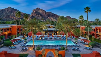 Zona de piscina en un resort con tumbonas, palmeras y montañas al fondo.