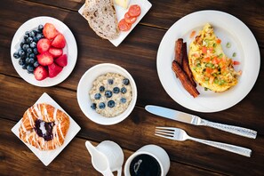 Een ontbijttafel met diverse etenswaren, waaronder toast, aardbeien, bosbessen, havermout, een omelet, spek en een croissant.