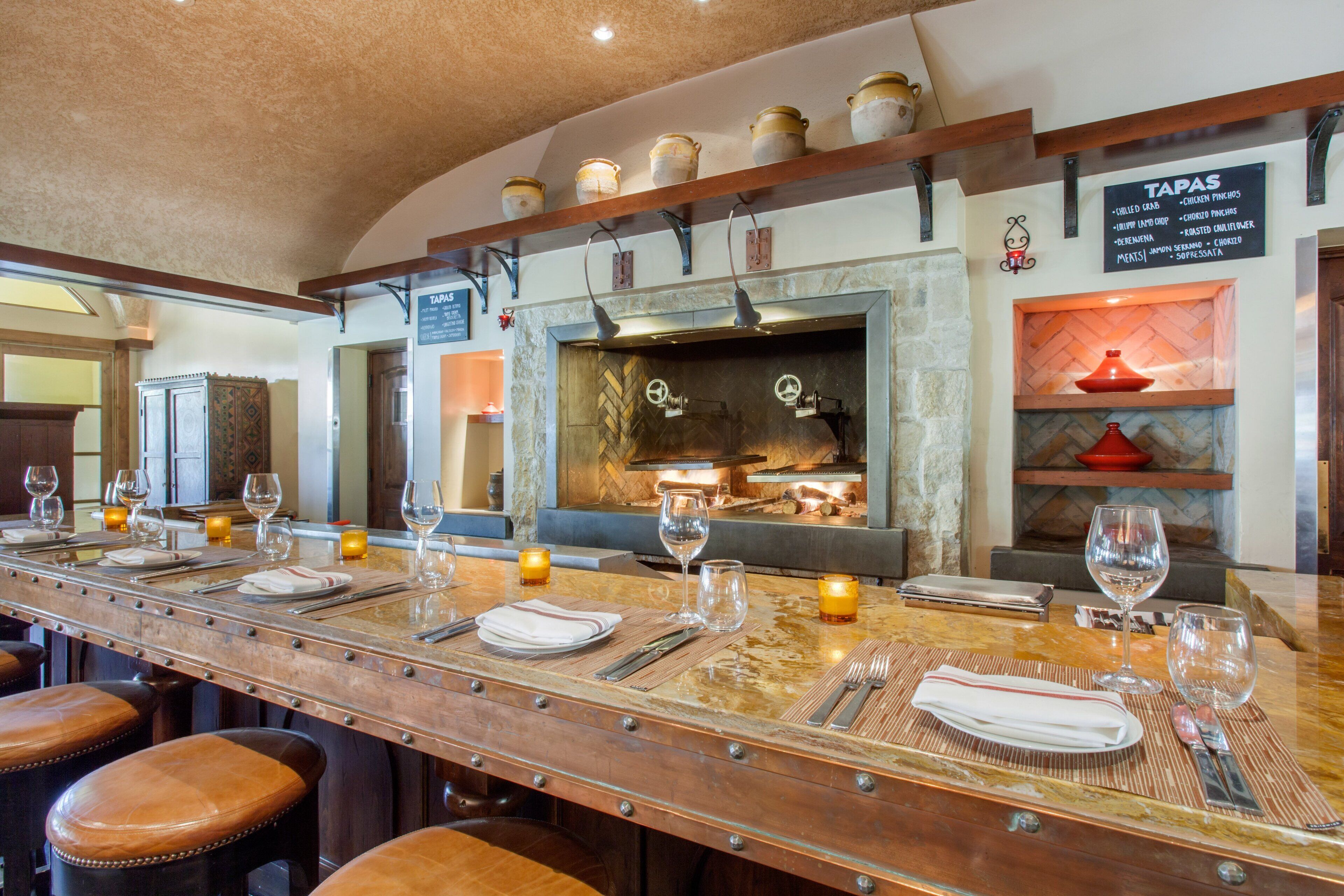 A bar area with a long counter, stools, and a menu board listing tapas.
