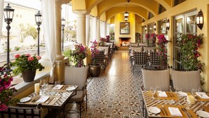 Een restaurant met terras, witte gordijnen en plantenpotten.