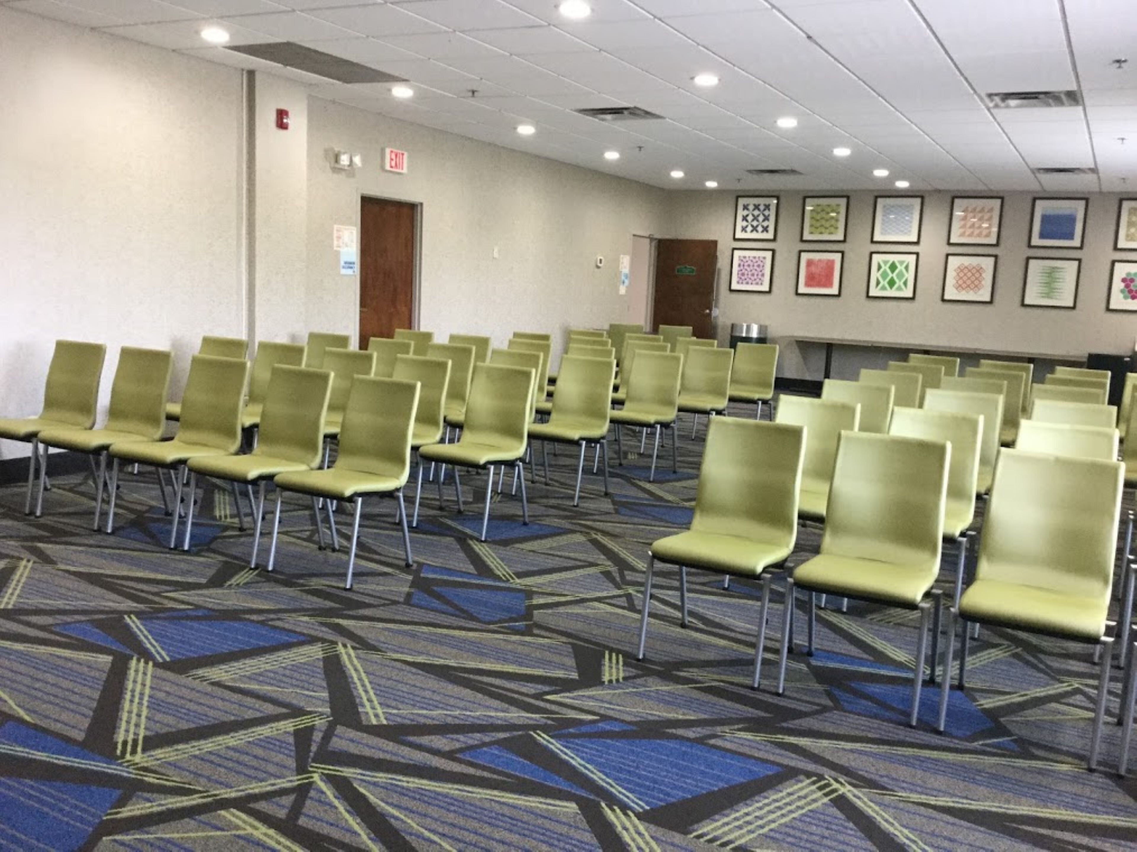 A conference room with rows of green chairs, a patterned carpet, and framed pictures on the wall.