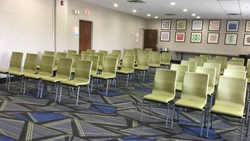 A conference room with rows of green chairs, a patterned carpet, and framed pictures on the wall.