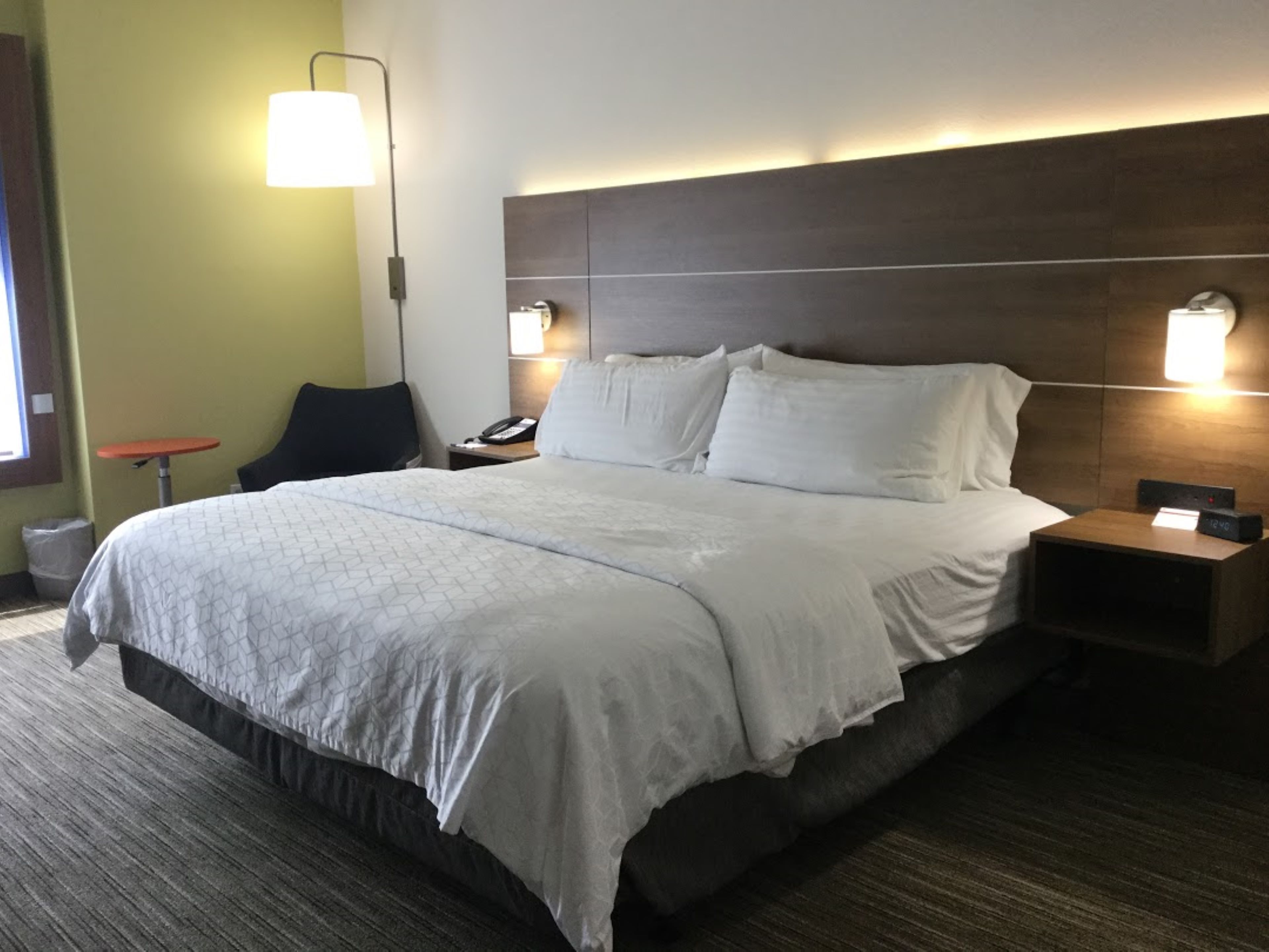 Une chambre d’hôtel avec un grand lit, deux tables de chevet, une petite table, une chaise et une lampe.