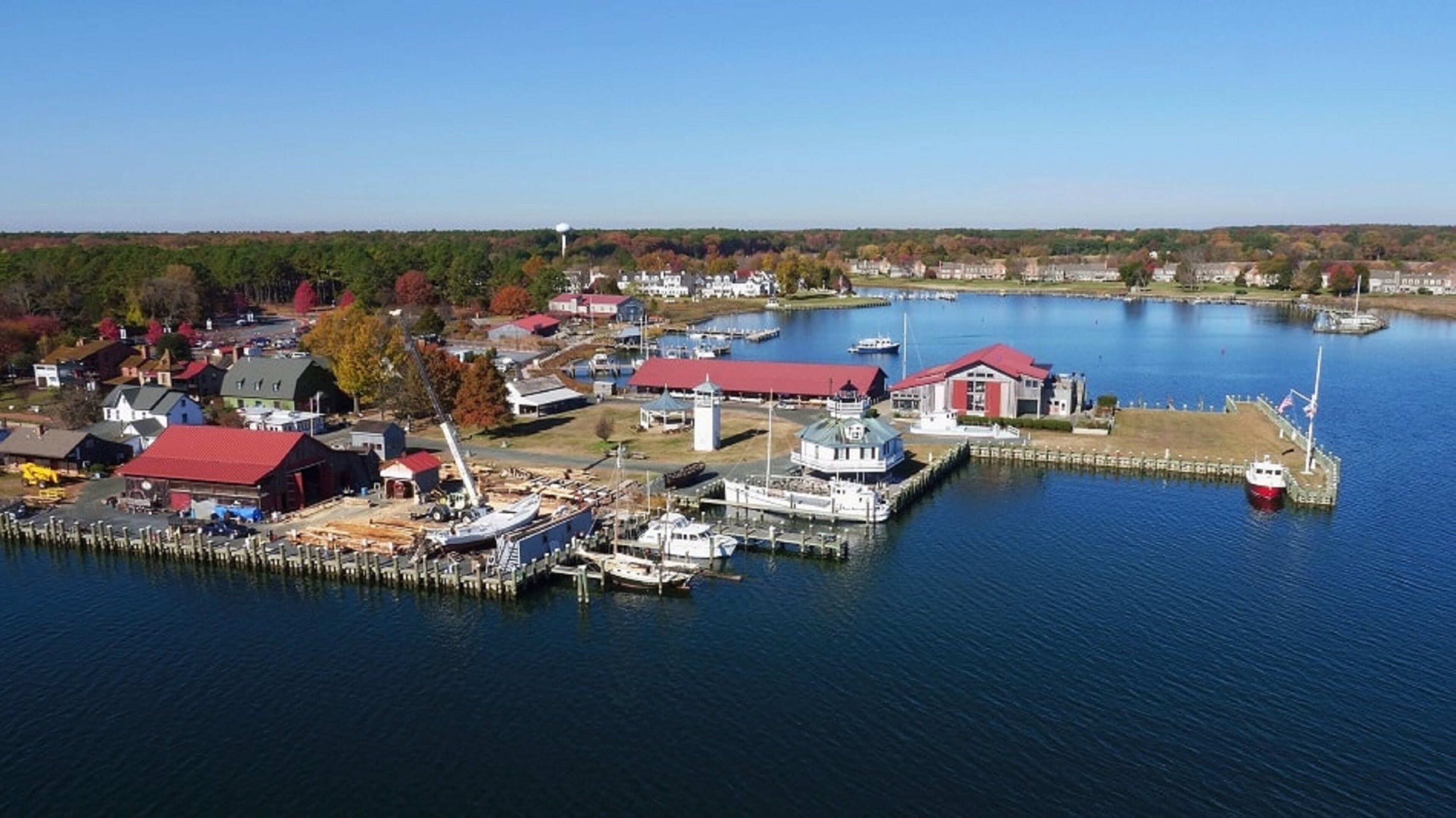A marina with boats docked, a lighthouse, and buildings with red roofs.
