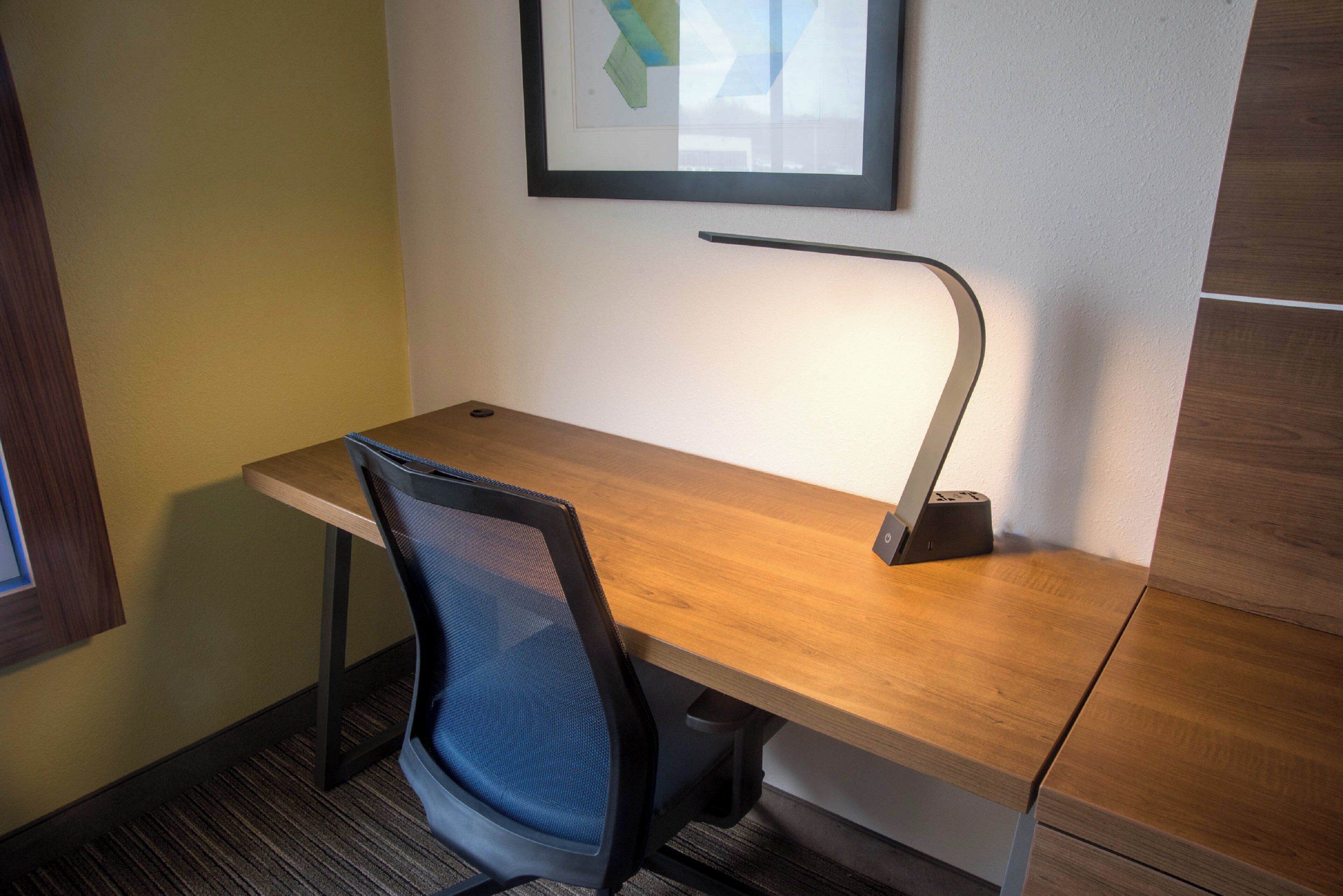 A modern office desk with a chair, a desk lamp, and a framed picture on the wall.