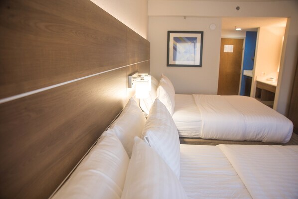 Ein Hotelzimmer mit zwei Betten, einem Holzkopfteil, einem Nachttisch mit Lampe und einem gerahmten Bild an der Wand.