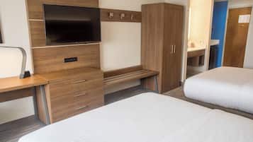 Quarto de hotel com cama, escrivaninha, televisão de tela plana, armário e banheiro visível através de uma porta aberta.