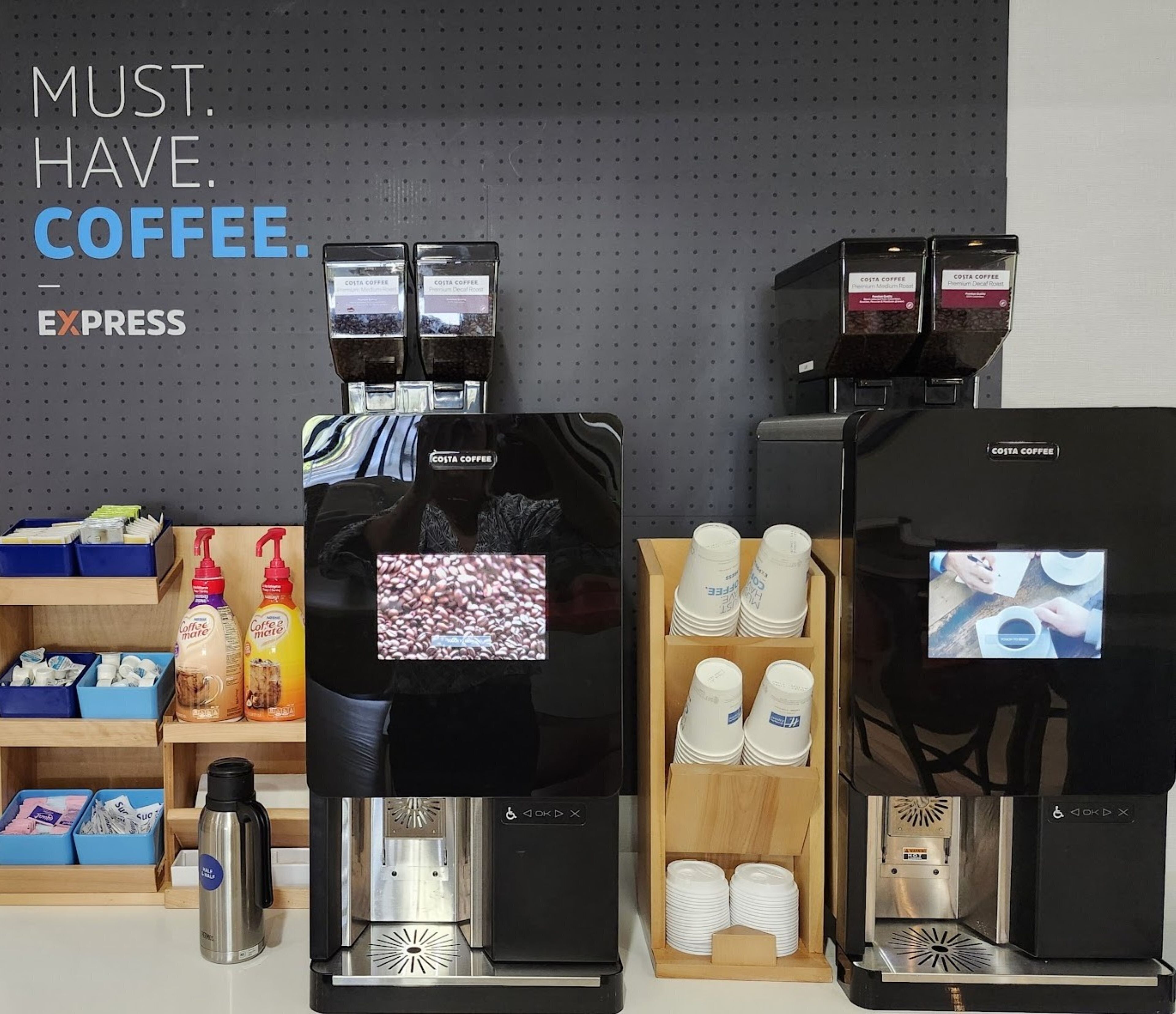 Una estación de café con varios dispensadores, una máquina de café y una presentación de vasos desechables.