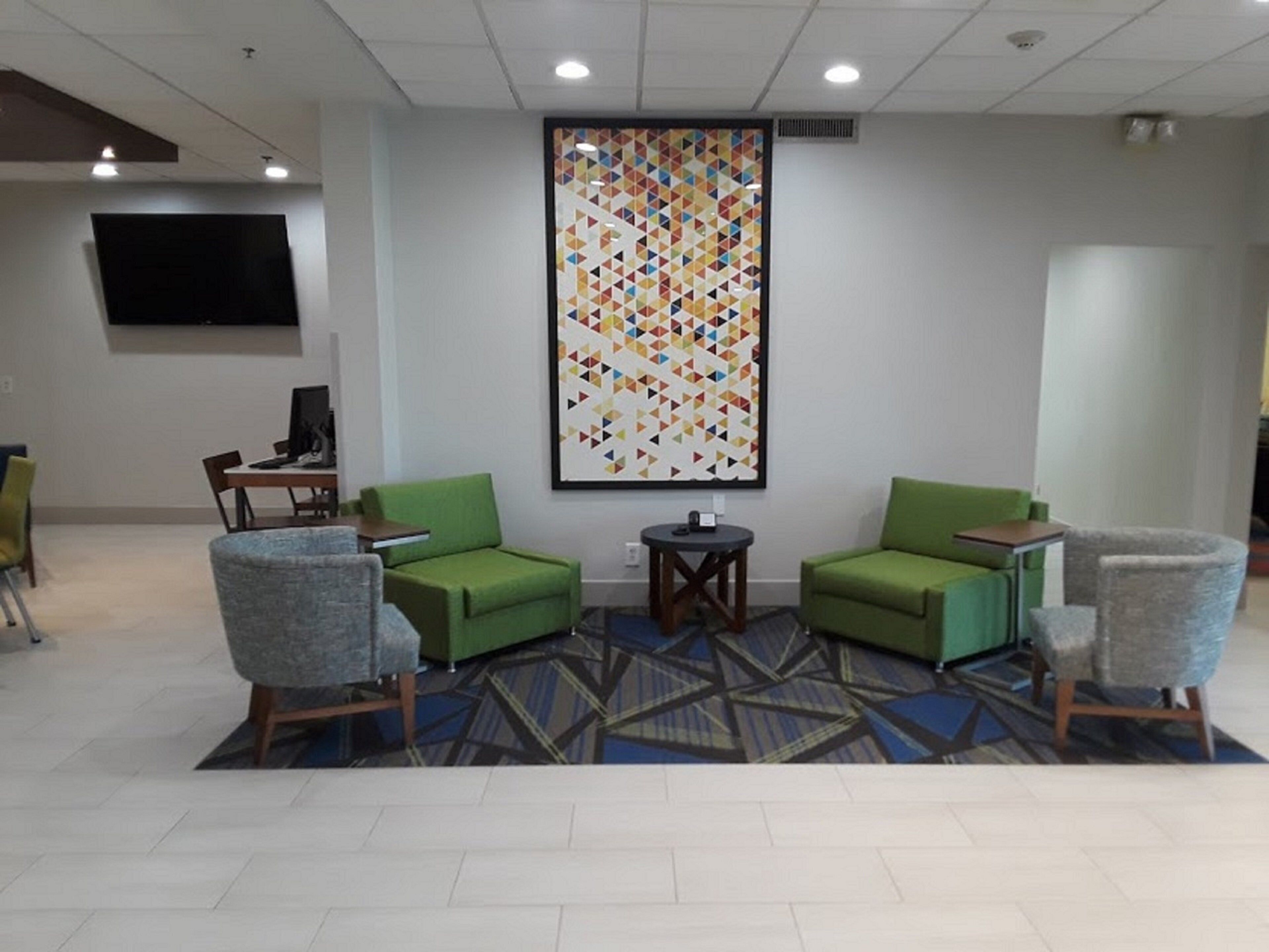 Un hall con dos sillones verdes, una mesita redonda, un televisor de pantalla plana montado en la pared y una alfombra estampada.