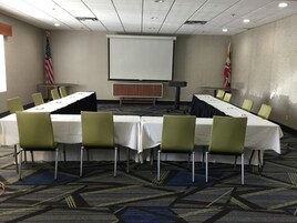 Un salón de conferencias con una larga mesa, sillas, una pantalla de proyector y dos banderas.