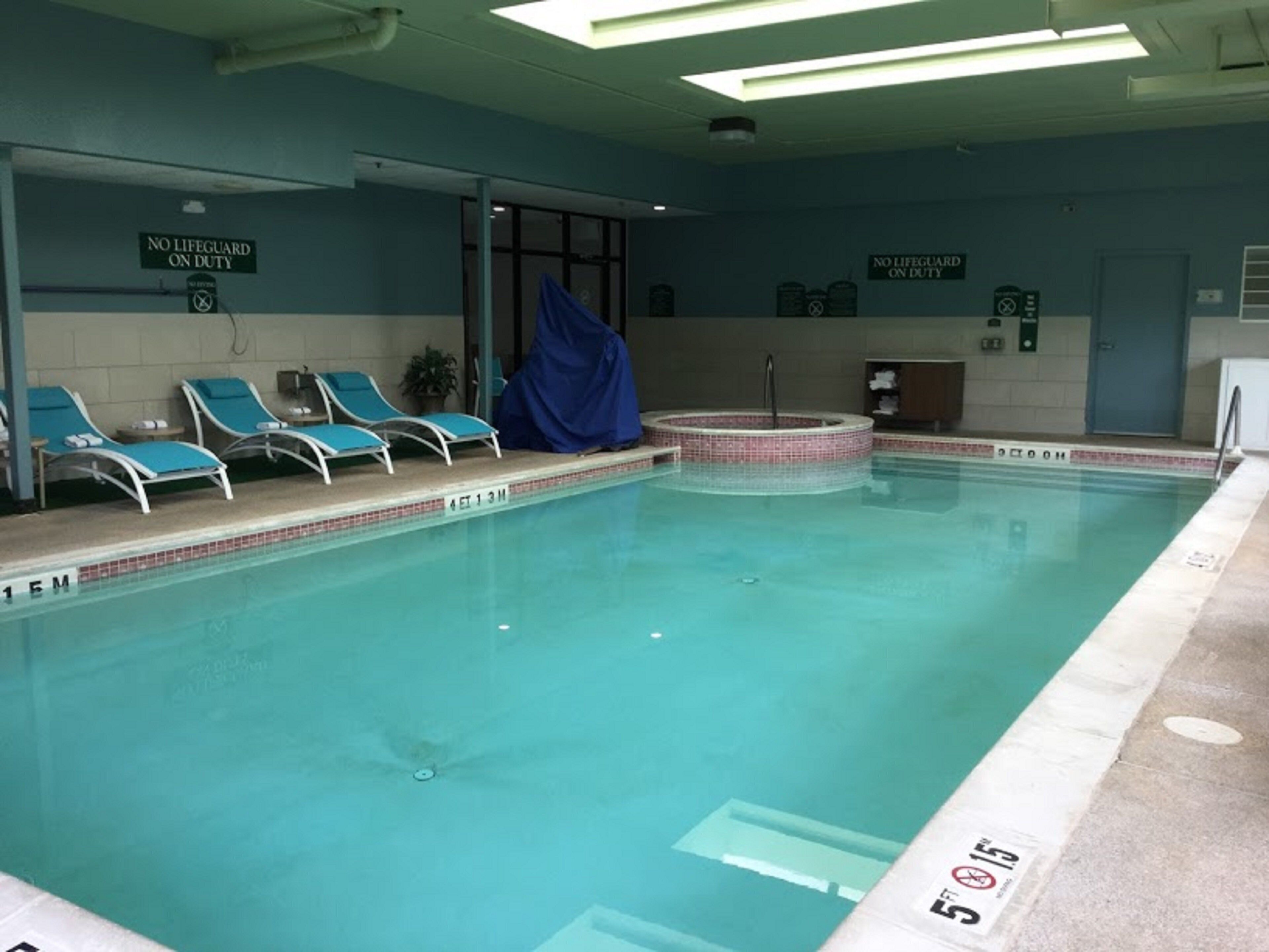 An indoor swimming pool with lounge chairs and a hot tub.