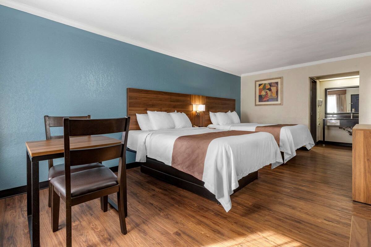 A hotel room with two beds, a wooden desk, and a chair.