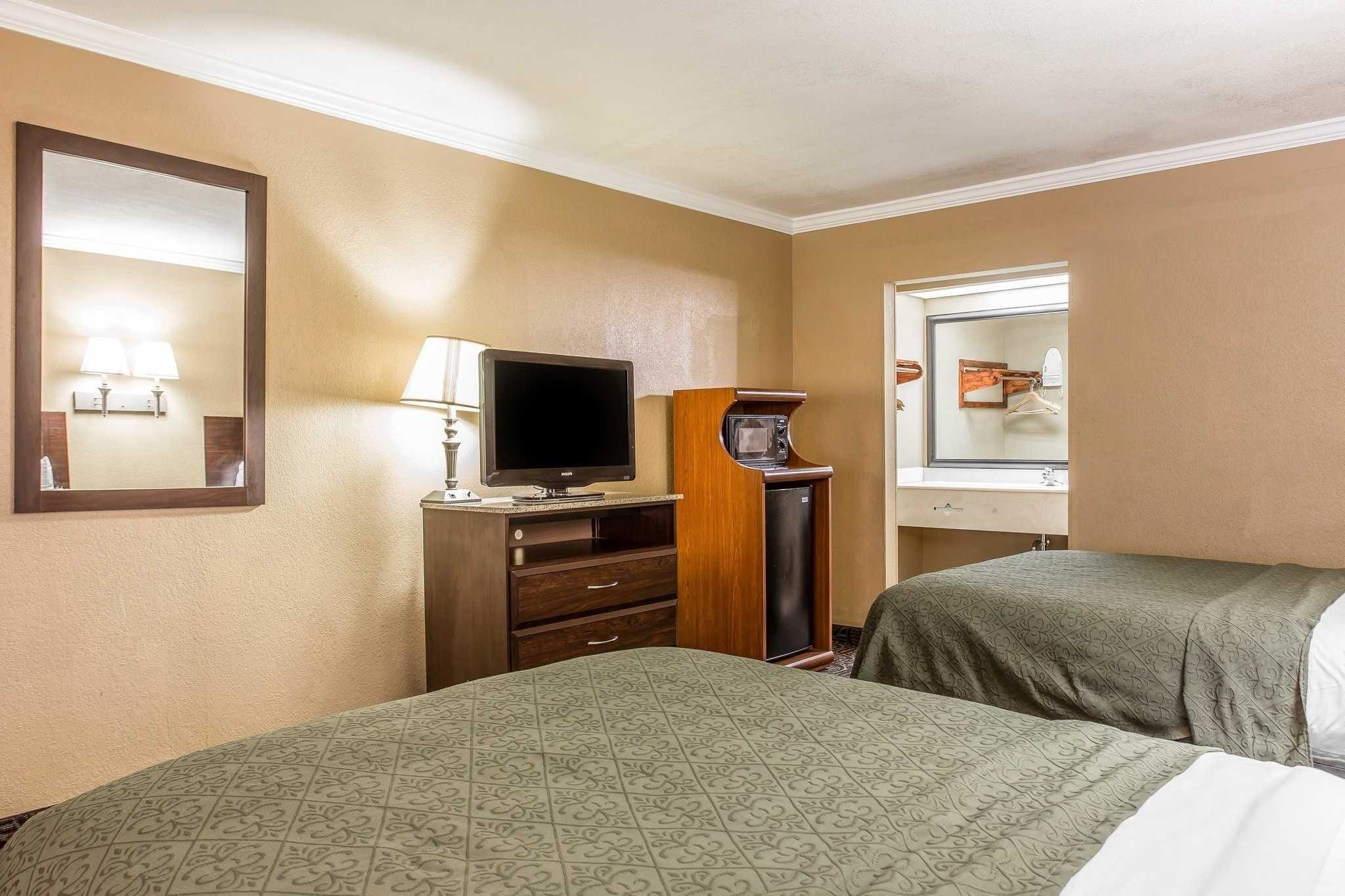 A hotel room with two beds, a TV, a desk with a lamp, and a mirror.