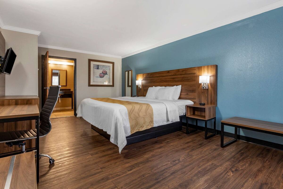 A hotel room with a bed, desk, chair, bedside tables, and a TV.
