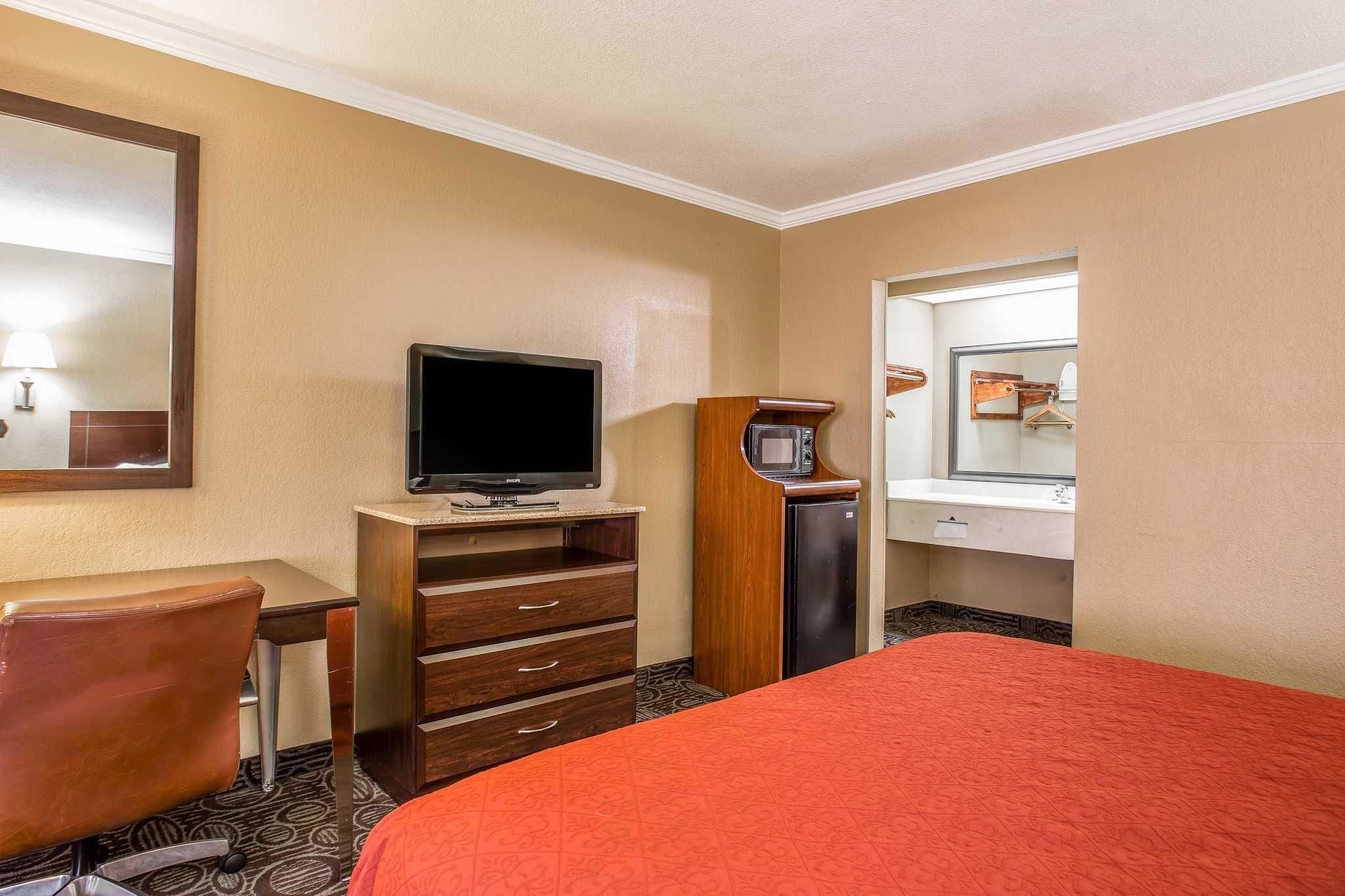 A hotel room with a bed, a desk with a television, a microwave, and a mirror.