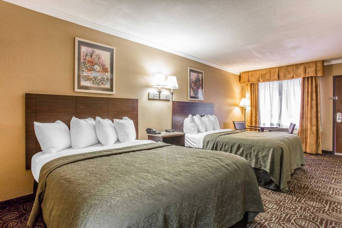 A hotel room with two beds, a nightstand, a lamp, and a painting on the wall.