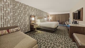 Una habitación de hotel con alfombra estampada, una cama, un escritorio, una silla y un televisor.