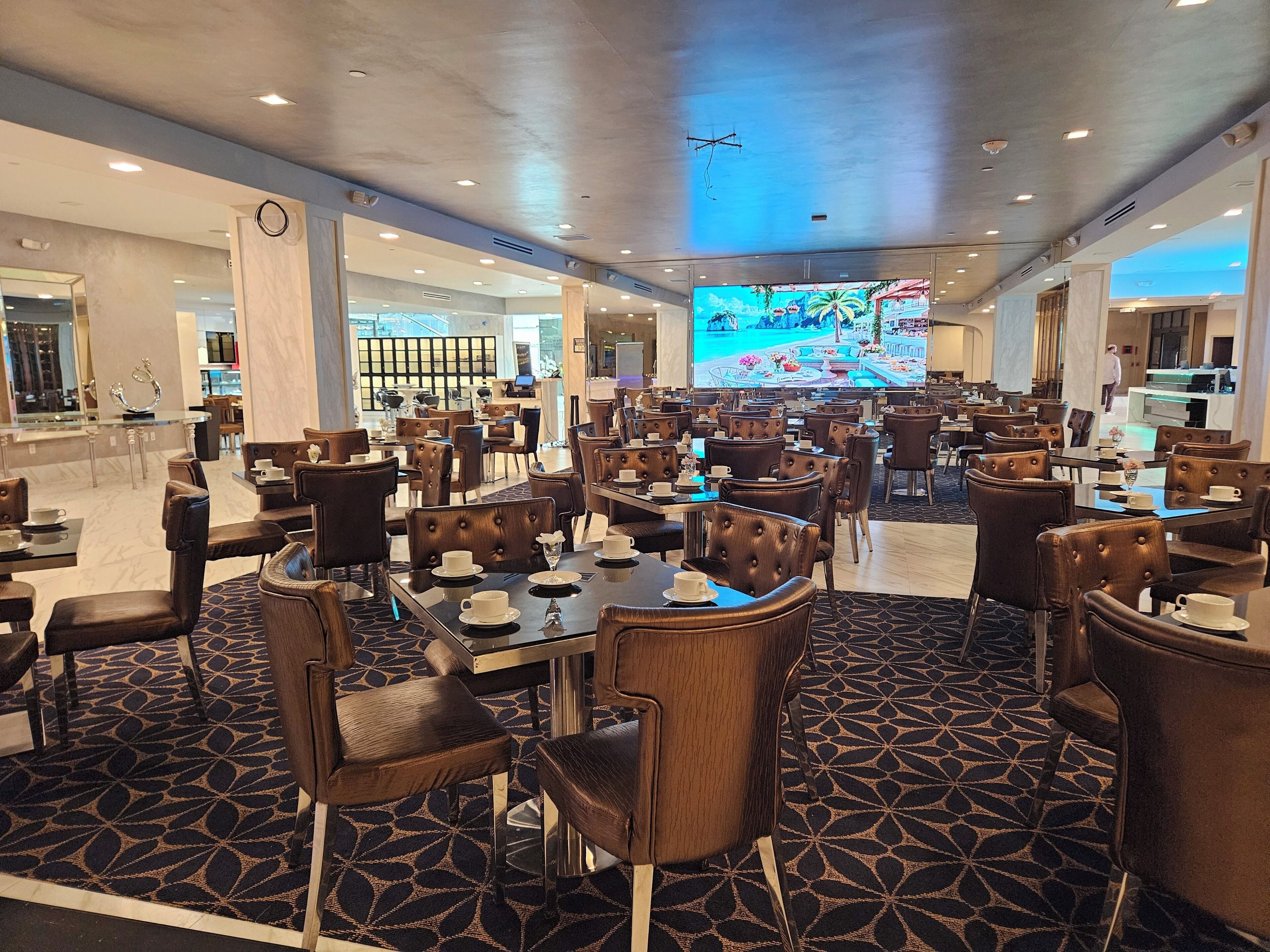 Un restaurant spacieux avec des tables et des chaises hautes, un grand écran de télévision et une moquette à motifs.