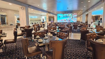 Un restaurant spacieux avec des tables et des chaises hautes, un grand écran de télévision et une moquette à motifs.