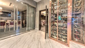 A modern interior with a glass door leading to a dining area, a wine cellar with glass shelves, and a marble floor. - Grand Tuscany Hotel (Houston)