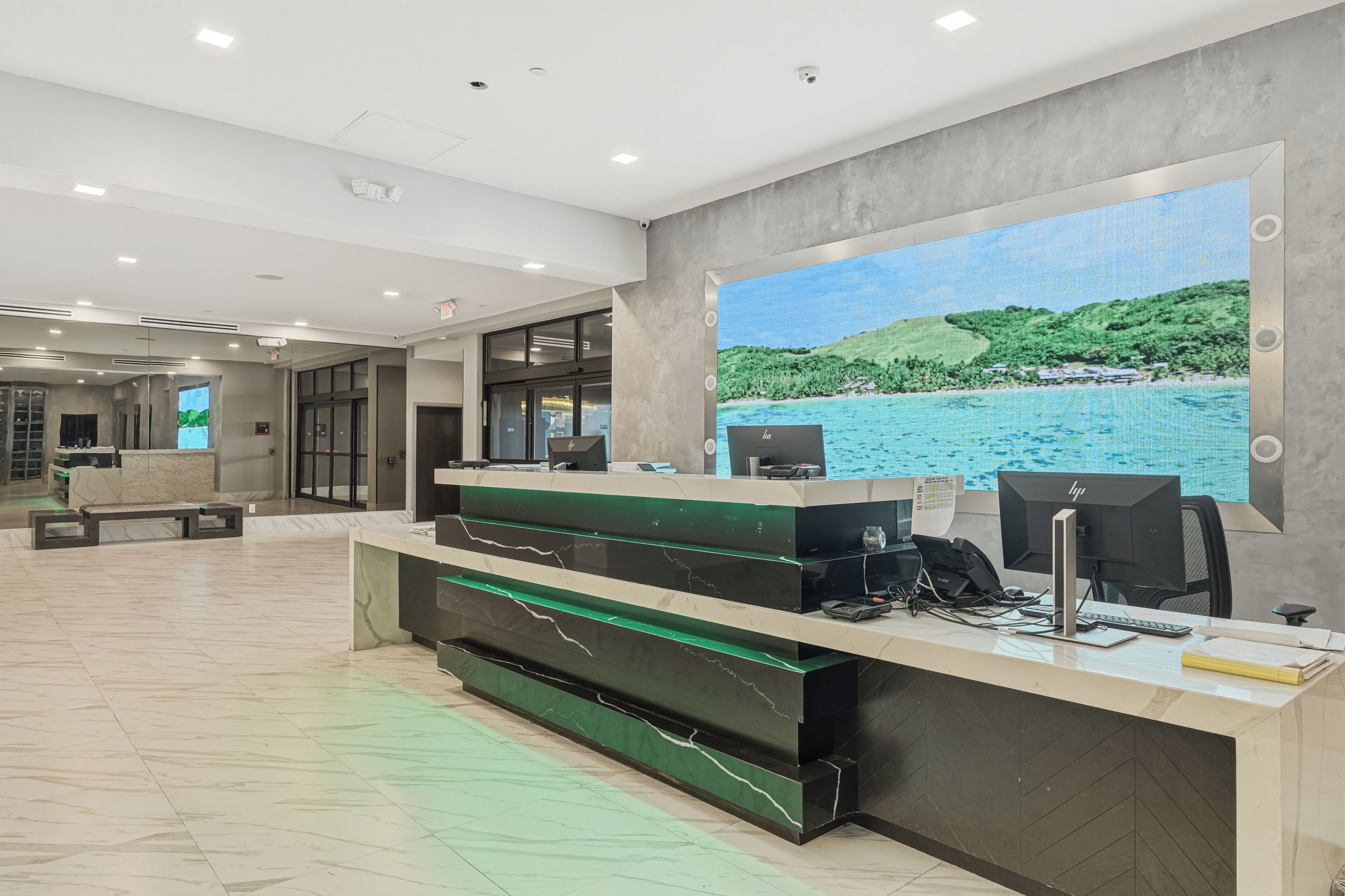 A reception desk with a large window displaying a coastal landscape, a modern interior with a marble floor, and a reception area with a counter and seating.