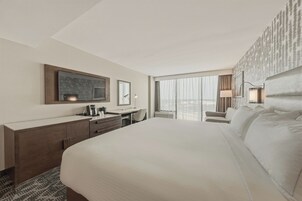 Une chambre d’hôtel avec un grand lit, un bureau avec une chaise, un minibar et une grande fenêtre donnant sur un beau paysage.