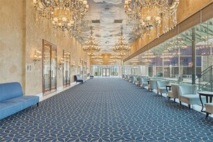 Un'ampia hall dell'hotel con tappeto decorato, file di posti a sedere e un sontuoso lampadario.
