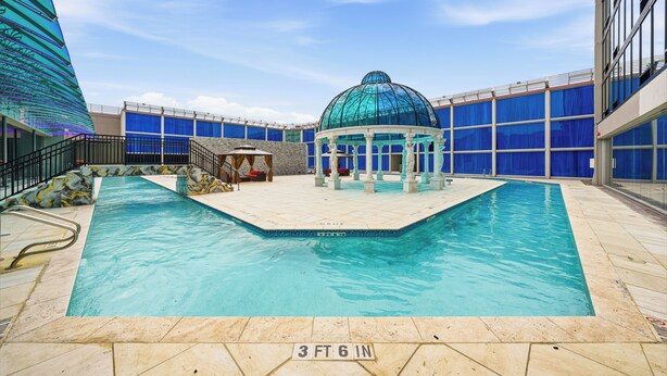 An indoor swimming pool with a glass-domed structure, surrounded by blue-tinted walls and a stone-tiled floor. - Grand Tuscany Hotel (Houston)