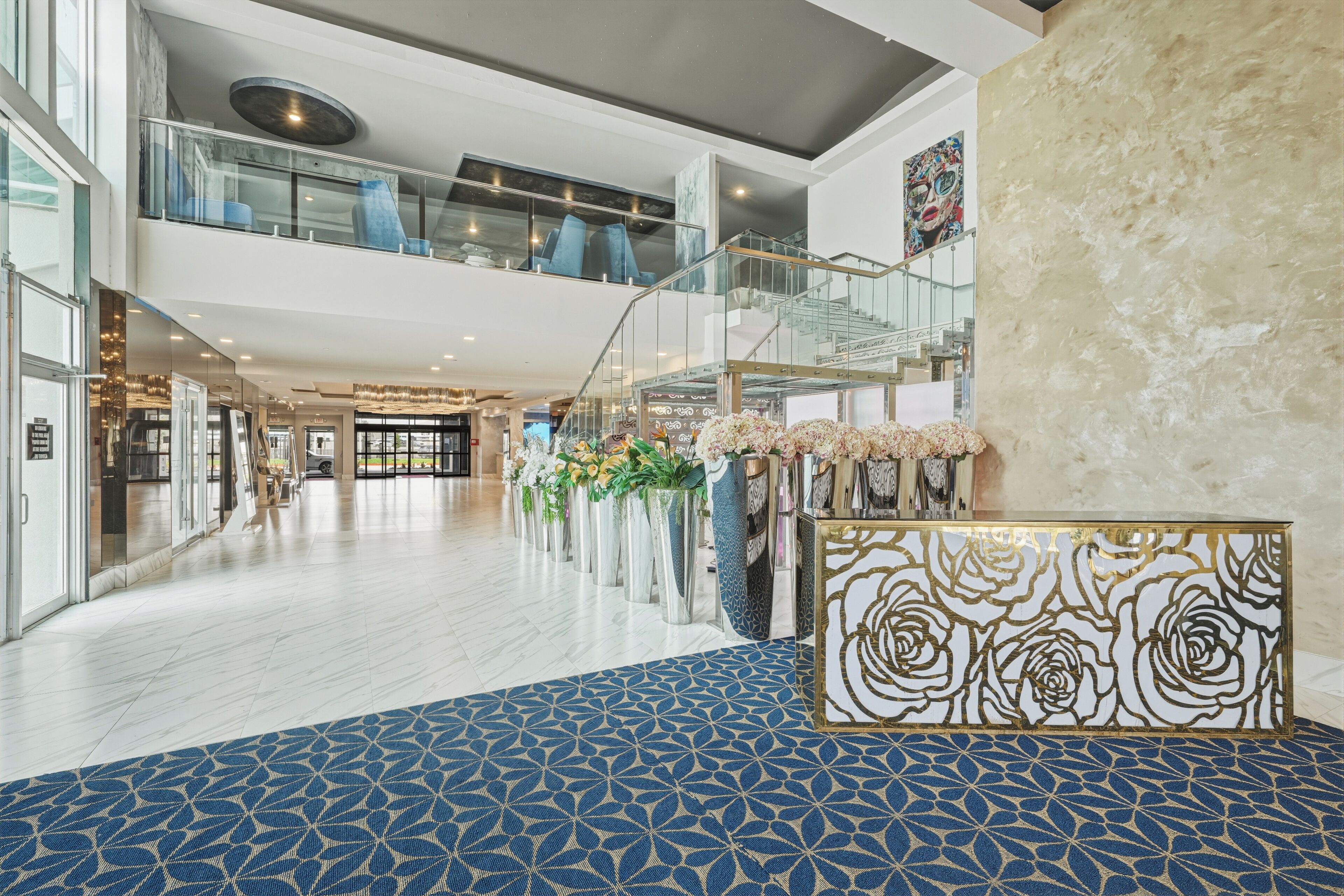 Un vestíbulo amplio con un carpeta de diseño azul, un arreglo floral central y una escalera moderna.