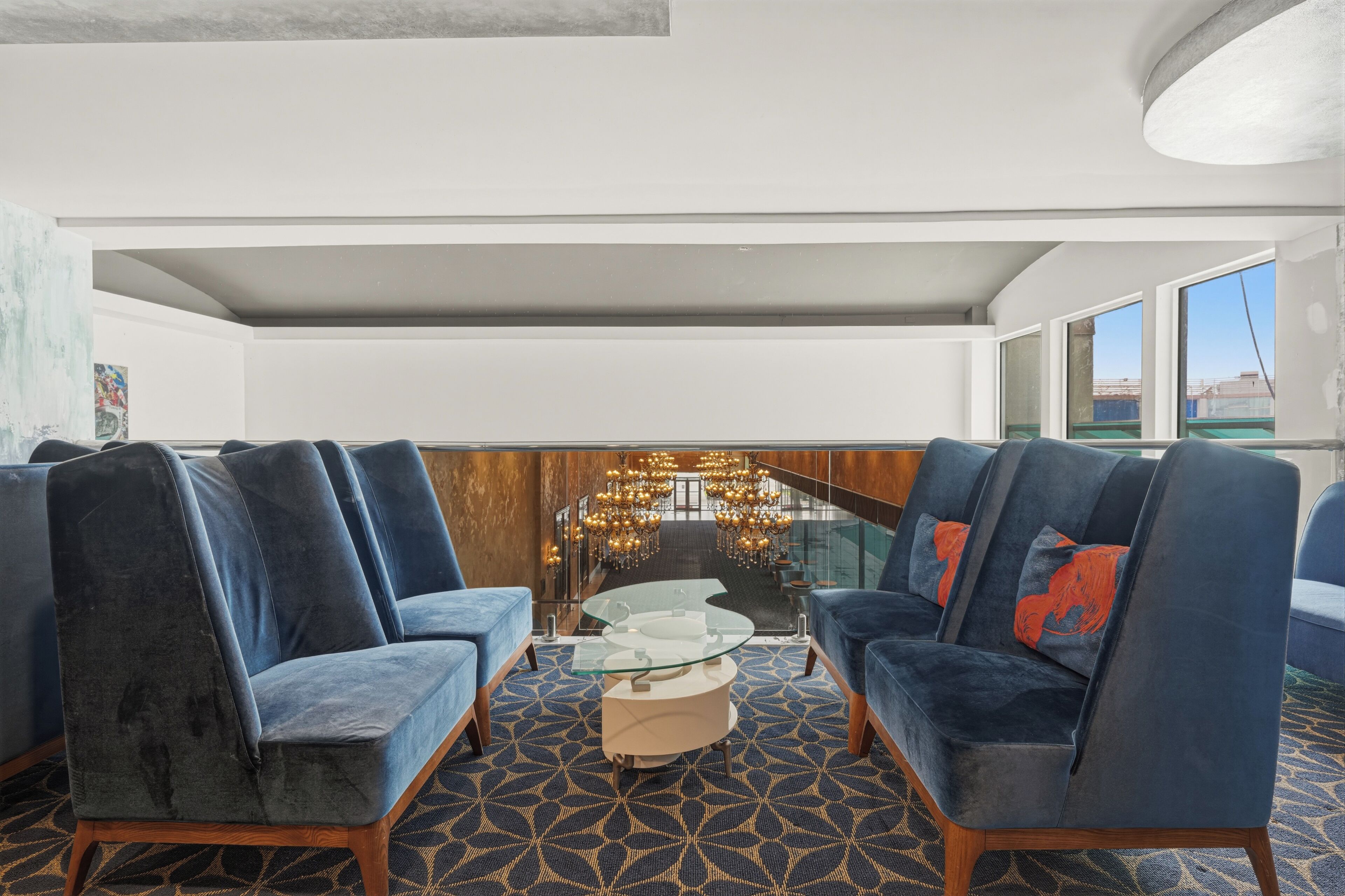 A modern lounge area with a glass coffee table, blue upholstered sofas, and a patterned carpet.