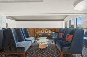 Uma área de estar moderna com uma mesa de centro de vidro, sofás estofados em azul e um tapete estampado.