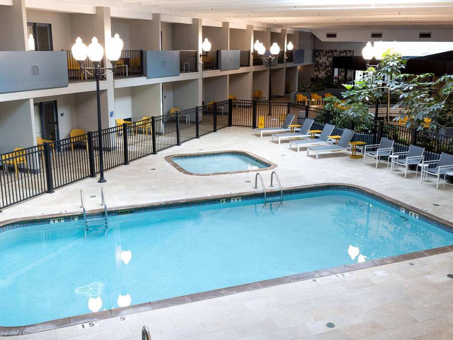 An indoor swimming pool with a tiled floor, lounge chairs, and a small hot tub.