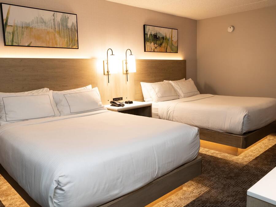 Habitación de hotel con dos camas, una mesita de noche con teléfono y control remoto, y lámparas fijadas a la pared.
