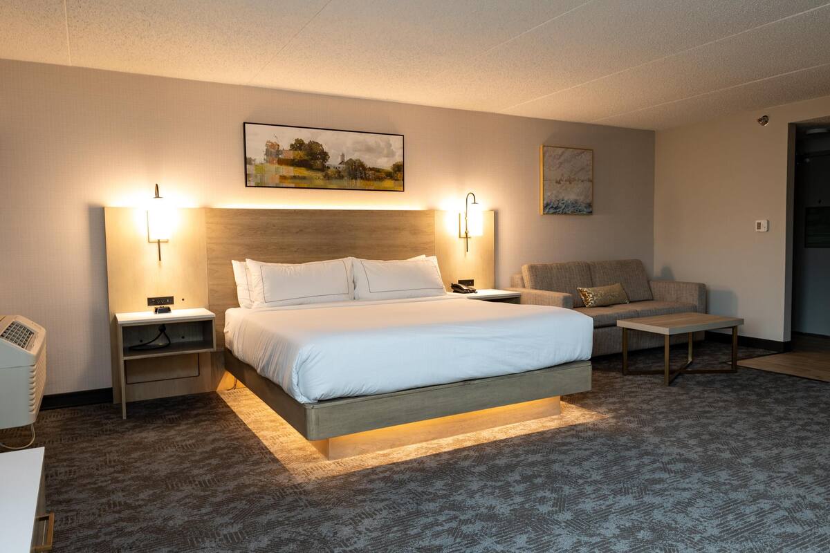 A hotel room with a large bed, two bedside tables, a sofa, and a small table.