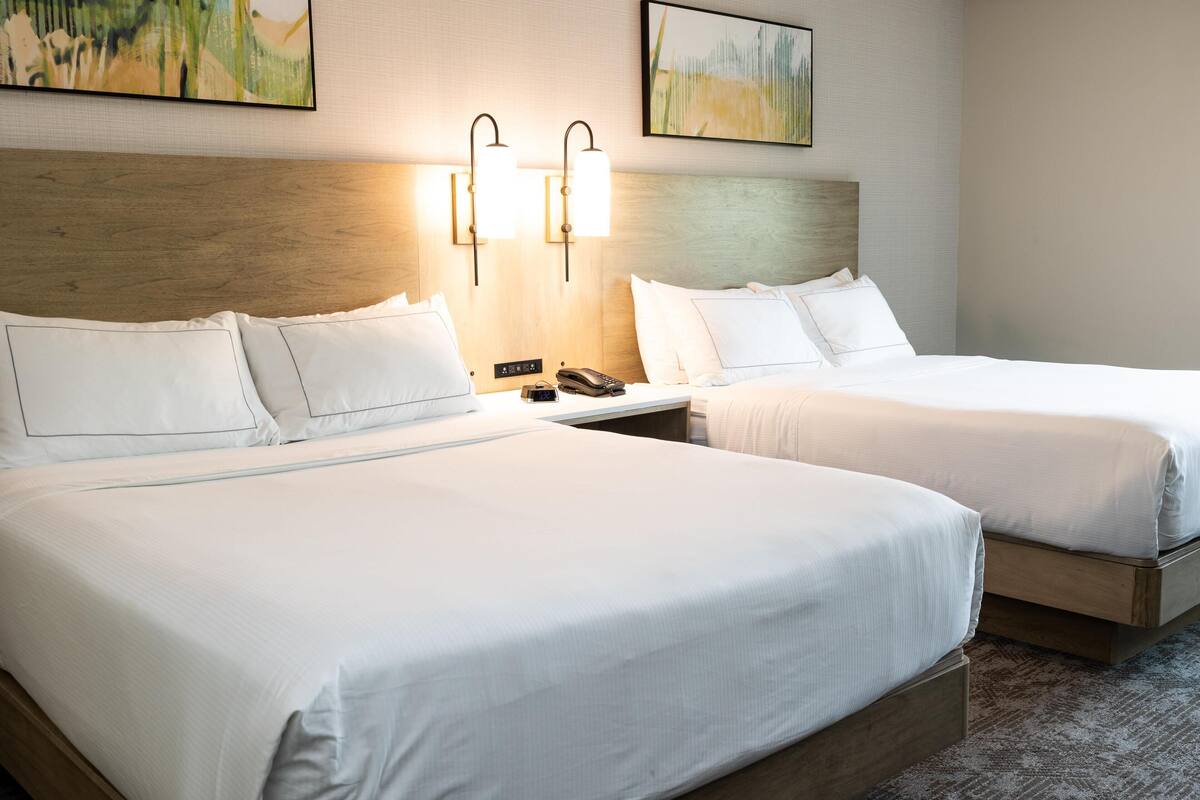 A hotel room with two beds, a wooden headboard, wall-mounted lights, and a telephone on the nightstand.