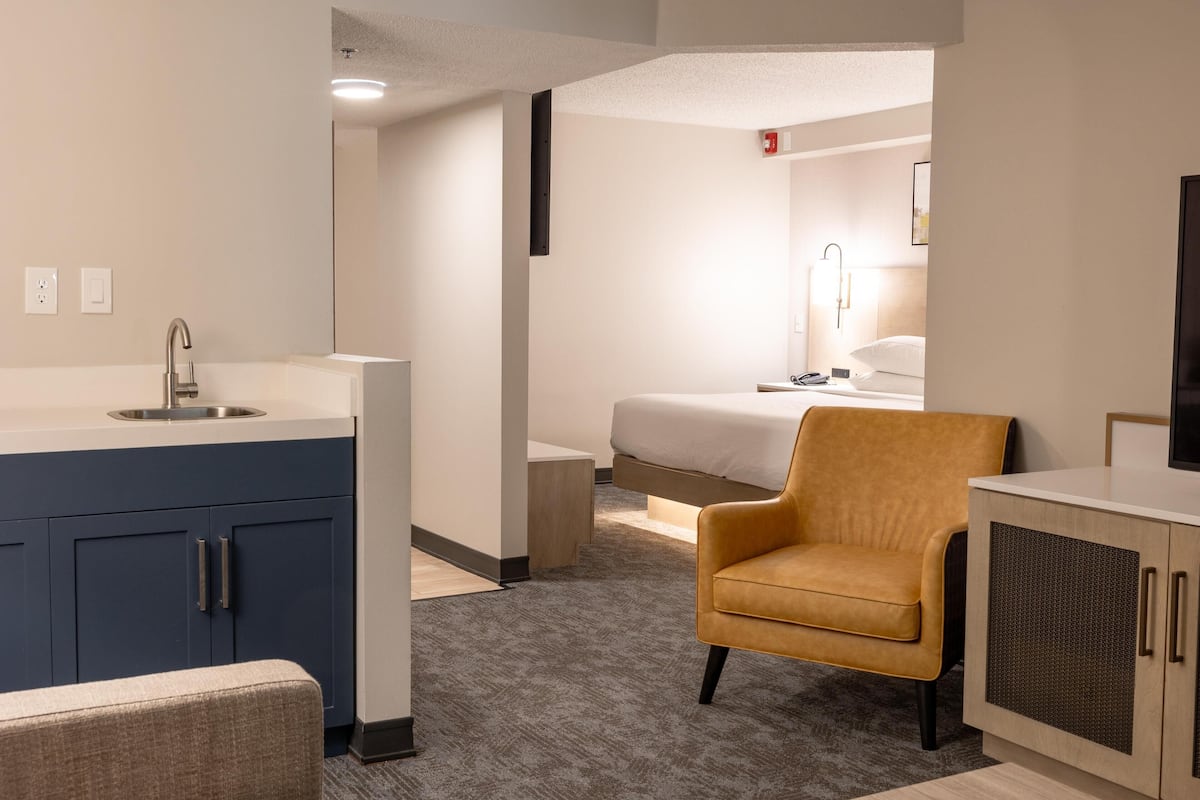 A modern hotel room with a bathroom, a bed, a sofa, and a TV.