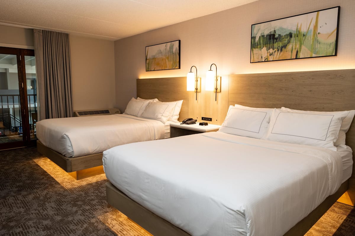 A hotel room with two beds, a wooden headboard, a nightstand with a phone, and artwork on the walls.