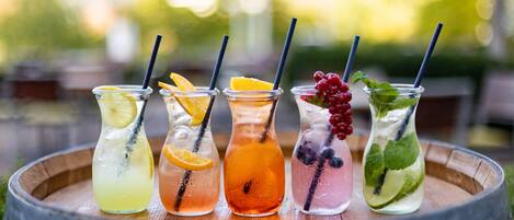 Five glass bottles of beverages with straws, placed on a wooden tray.