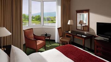 Une chambre d’hôtel équipée d’un lit, d’un bureau, d’une chaise, d’une télévision et offrant une vue sur un lac et des montagnes.