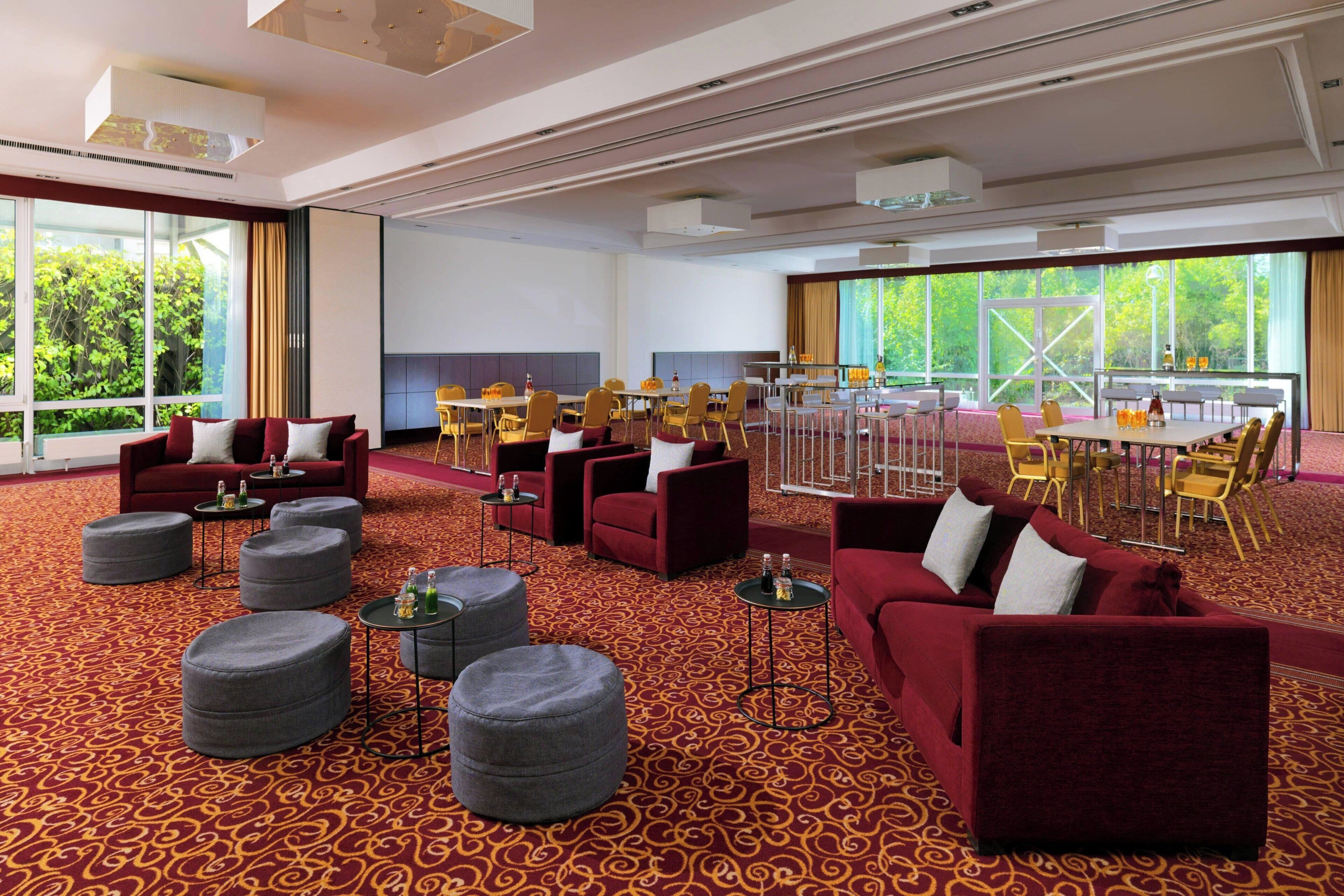 A spacious hotel lobby with red sofas, round ottomans, and a dining area with yellow chairs.
