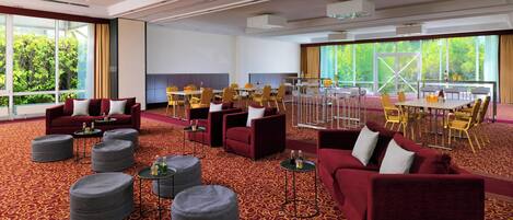 A spacious hotel lobby with red sofas, round ottomans, and a dining area with yellow chairs.