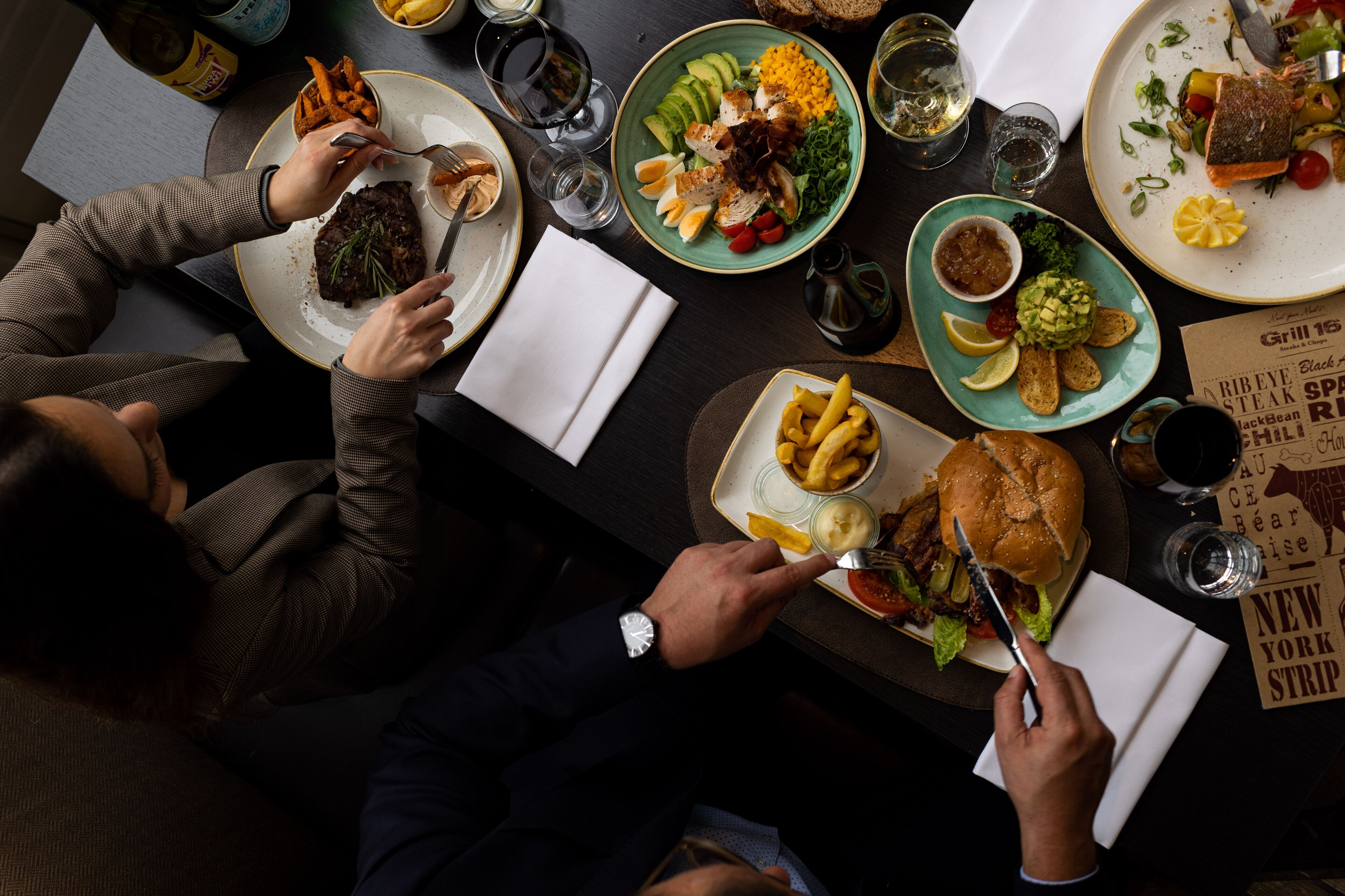 Ein Esstisch mit verschiedenen Speisen, darunter Steak, Salat und Pommes.