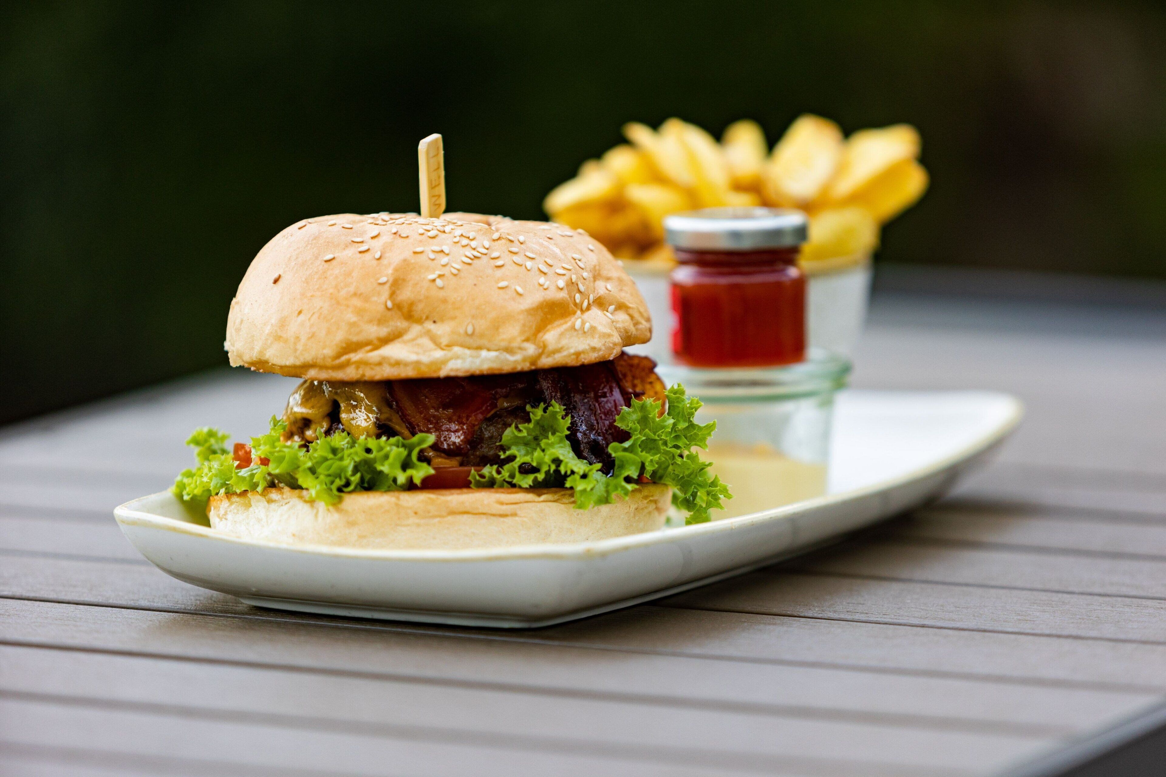 Un plato con una hamburguesa, papas fritas y un frasco pequeño de kétchup.