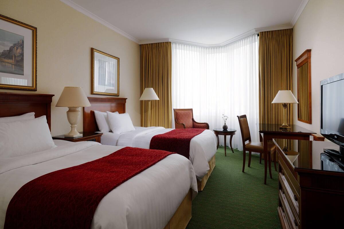 A hotel room with two beds, a desk, a chair, and a television.