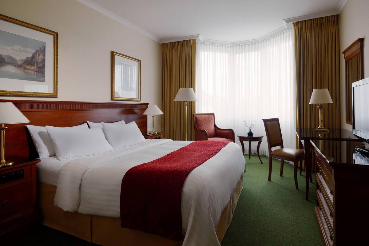 A hotel room with a large bed, two chairs, a desk, and a television.