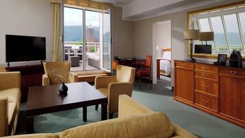 Habitación de hotel con televisión, sofá, mesa de comedor y balcón con vistas.