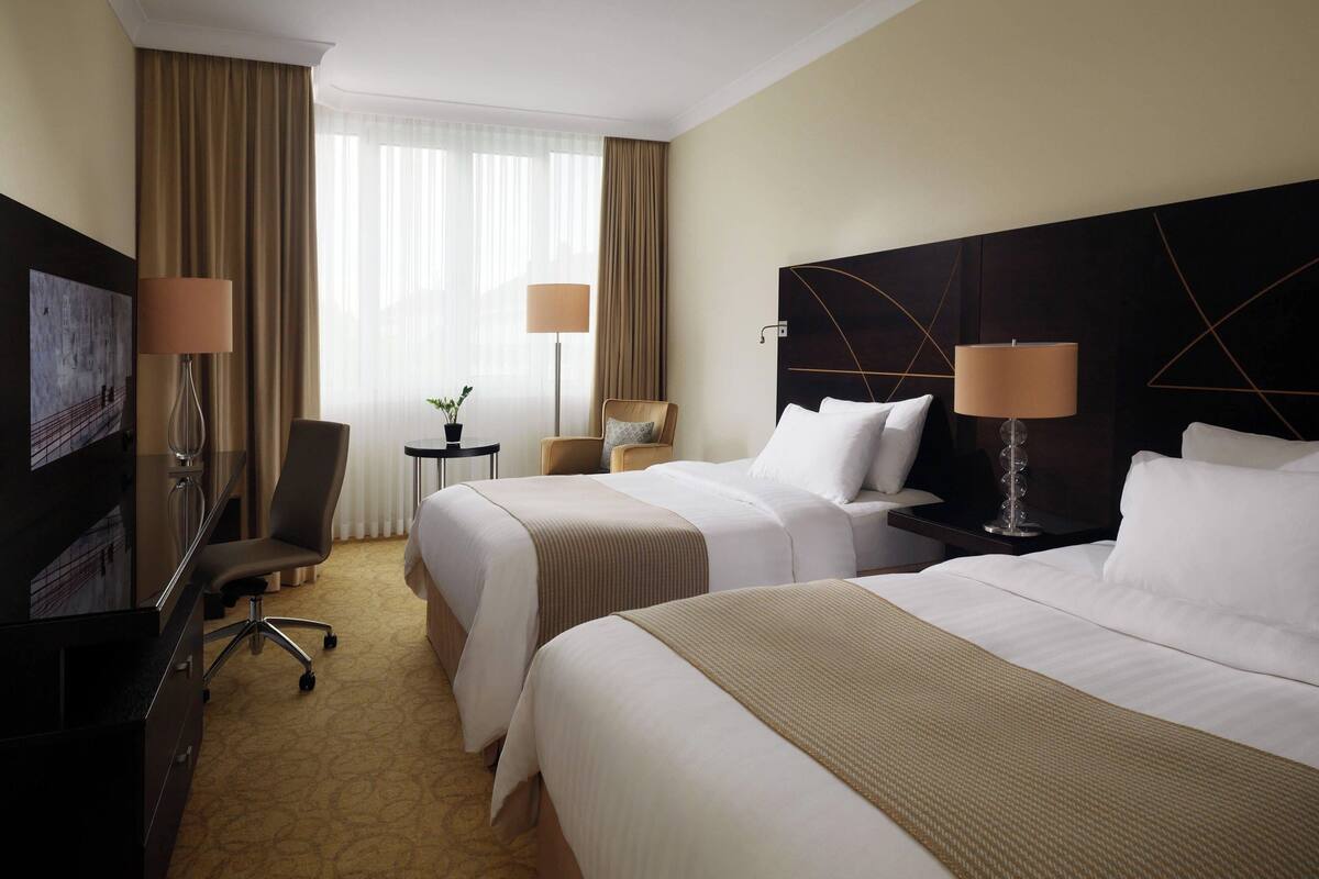 A hotel room with two beds, a desk, a chair, and a television.