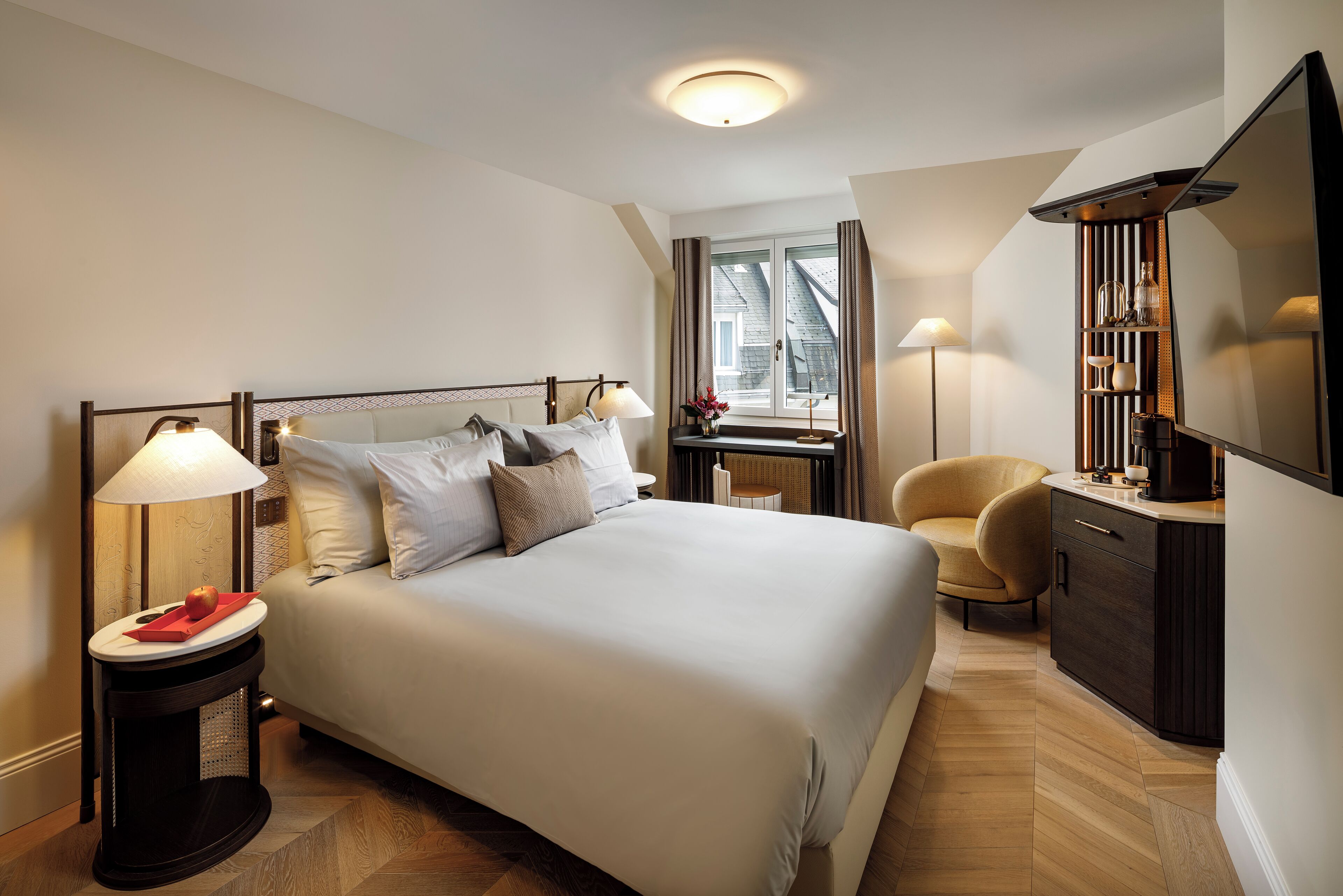 A neatly arranged bedroom with a large bed, bedside lamps, a chair, and a TV.