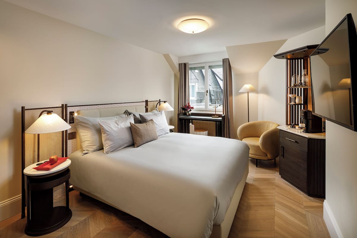 A neatly arranged bedroom with a large bed, bedside lamps, a chair, and a TV.
